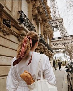 a woman is walking down the street with a bag in front of the eiffel tower