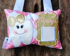 a pink and gold tooth fairy pillow hanging on a wooden wall