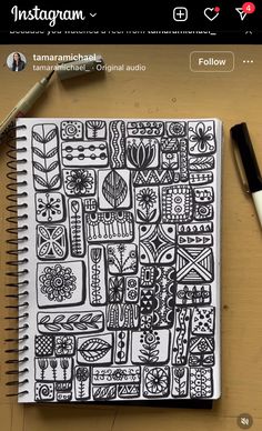 an open notebook with black and white doodles on the cover next to a pen