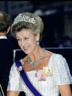 an older woman in a tiara smiles as she sits next to a young man