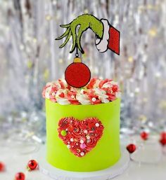 a green cake with red and white frosting on it, topped with a hand holding an ornament