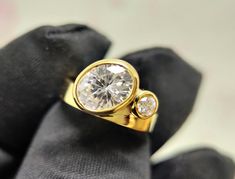 a yellow gold ring with two diamonds on it's side, sitting on a black cloth