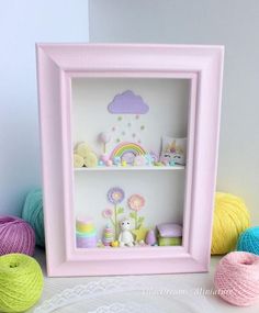 there is a pink shadow box with crochet toys in it and balls of yarn on the floor