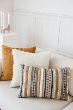 three decorative pillows on a white couch with candles in the background and one striped pillow