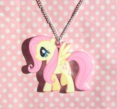 a pink pony with blue eyes is hanging from a silver necklace on a polka dot background