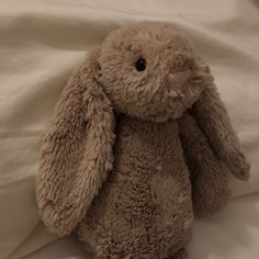 a stuffed animal sitting on top of a white sheet covered bed next to a pillow