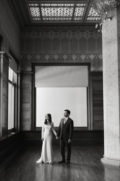 black and white photograph of a bride and groom holding hands in an empty room with columns