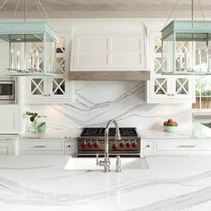 a kitchen with marble counter tops and white cabinets, an island in the middle is surrounded by hanging lights