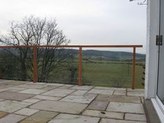 a balcony with stone flooring and wooden railings overlooking a green field in the distance