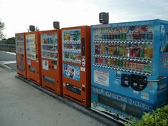 an orange and blue vending machine sitting next to each other on the side of a road