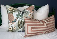 two decorative pillows on a bed with white linens and green headboard in the background