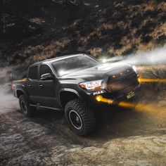 a truck driving down a dirt road with fog coming off the side of it's tires