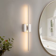 a white wall mounted light next to a mirror and potted plant on a table