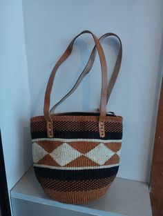 Geometrical earth tone sisal tote bag. Unique and stylish colorful sisal kiondo bag with stitched leather straps, pocket lining and zipper. Patterns and sizes slightly vary because weaving and stiching is done by hand. Ideal as a beach bag, shopping basket, market basket or storage basket. This unique tote bag is handmade by a group of ladies in a remote rural village in Machakos, Kenya. Do not clean with brush or water. If the bag gets wet, please dry to avoid dampness.  Leather type used is bo Shopping Basket Shoulder Bag With Leather Handles, Travel Handwoven Brown Hobo Bag, Woven Shoulder Satchel For Market, Multicolor Handheld Bags With Leather Handles, Brown Leather-handled Basket Bags, Brown Basket Shoulder Bag With Adjustable Strap, Brown Beach Shoulder Bag With Leather Handles, Beige Basket Bag With Handles, Everyday Use Basket Shoulder Bag With Adjustable Strap