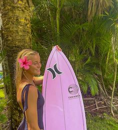 a woman holding a pink surfboard next to a palm tree