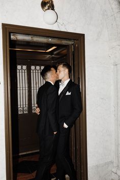 two men in tuxedos kissing each other at the entrance to an apartment building