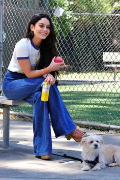 a woman sitting on a bench next to a white dog with an apple in her mouth