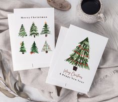 two christmas cards sitting on top of a blanket next to a cup and saucer