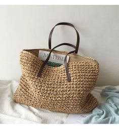 a straw bag sitting on top of a bed next to a book and magazine holder