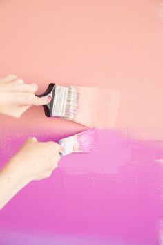 someone is painting a pink wall with a paintbrush in their hand and it looks like they are holding something