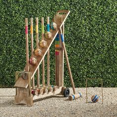 a wooden toy set with baseballs, bats and balls in front of a hedge