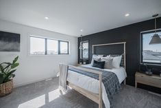 a bed room with a neatly made bed next to two windows and a potted plant