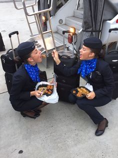 two women sitting on the ground eating out of their suitcases with food in front of them