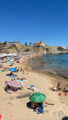 many people are on the beach and some have umbrellas over their heads while others swim in the water