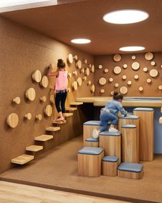 two children are climbing up the stairs in a playroom with wooden circles on the wall