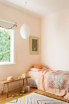 a bedroom with a bed, rug and table in front of a window that has a painting on the wall