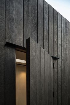 an open door on the side of a black building with wooden slatted walls