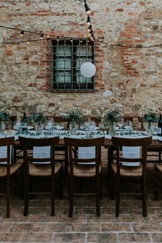 an outdoor dining table set up with white linens and greenery, surrounded by brick walls