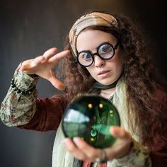 a woman wearing glasses holding a glass ball in her hand and looking at the camera