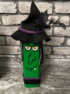 a green tube with a witches hat on it's head and feathers sticking out of the top