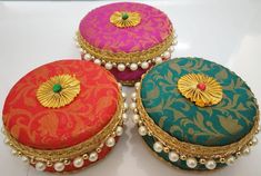 three colorful boxes with pearls on them sitting next to each other in front of a white table