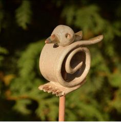 a bird figurine sitting on top of a wooden stick in front of some trees