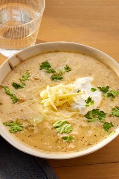 a bowl of soup with sour cream and parmesan cheese on top, next to a glass of water