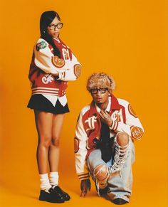 two people standing next to each other in front of an orange background with one person wearing glasses