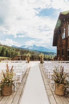 an outdoor ceremony setup with white chairs and flower baskets on the aisle, overlooking mountains