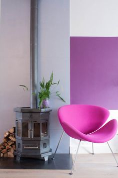 a pink chair sitting in front of a stove next to a pile of wood and a potted plant