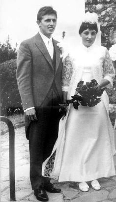 an old black and white photo of a man and woman in wedding attire standing next to each other