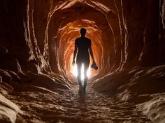 a man is walking through a tunnel with light coming from the end and his hand on his hip