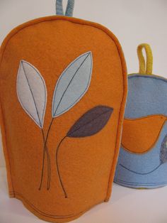 two pot holders made out of felt with leaves on the top and bottom, one in blue and orange