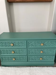 an old dresser painted green with gold handles and knobs on the drawers is sitting in front of a white rug