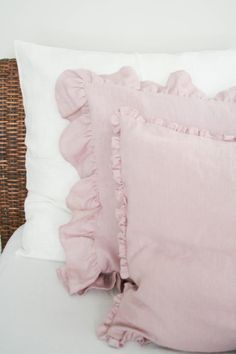 two pink pillows sitting on top of a white bed next to a wicker headboard