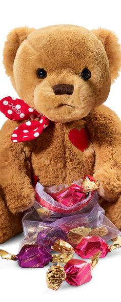 a brown teddy bear sitting on top of a pile of chocolates and candies