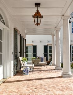 an outdoor patio with chairs and lamps on the ceiling, surrounded by white pillars that are lined with black shutters