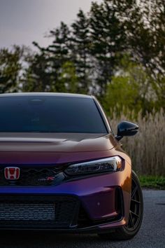 the front end of a purple and black car parked in a parking lot next to trees