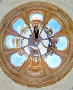 a woman is standing in the middle of a circular window with sky reflected on it