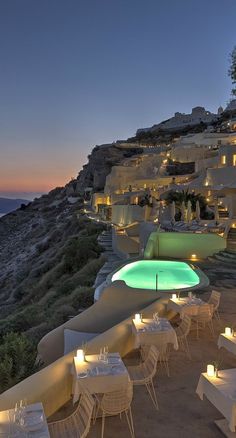 an outdoor dining area with tables and chairs overlooking the ocean at night, lit up by candles